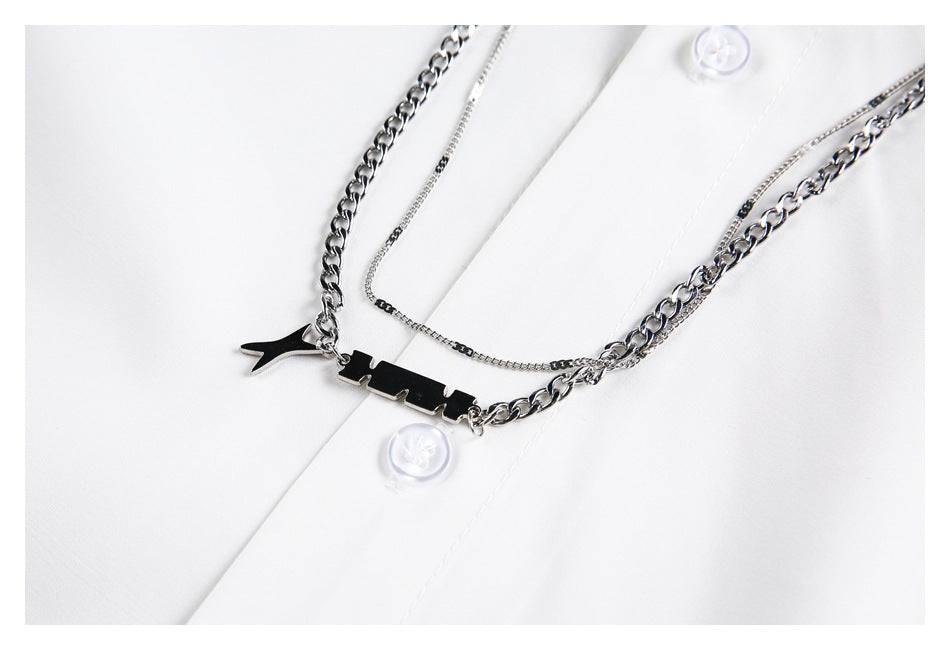 Close-up of layered silver chains and a black pendant draped across a white button-up shirt.