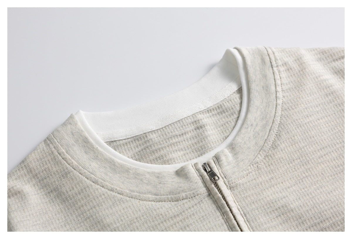 Close-up of a light heather-gray knit top's white crew neckline and short silver zipper.