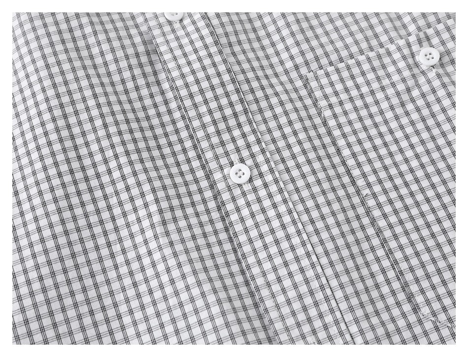 Close-up of a white shirt with a fine black grid check, showing white buttons, the placket and chest pocket.