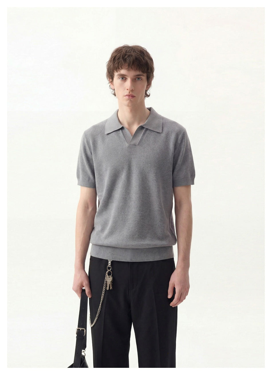 Model wearing a gray short-sleeve collared polo with a V-shaped opening and ribbed hem, paired with black trousers.