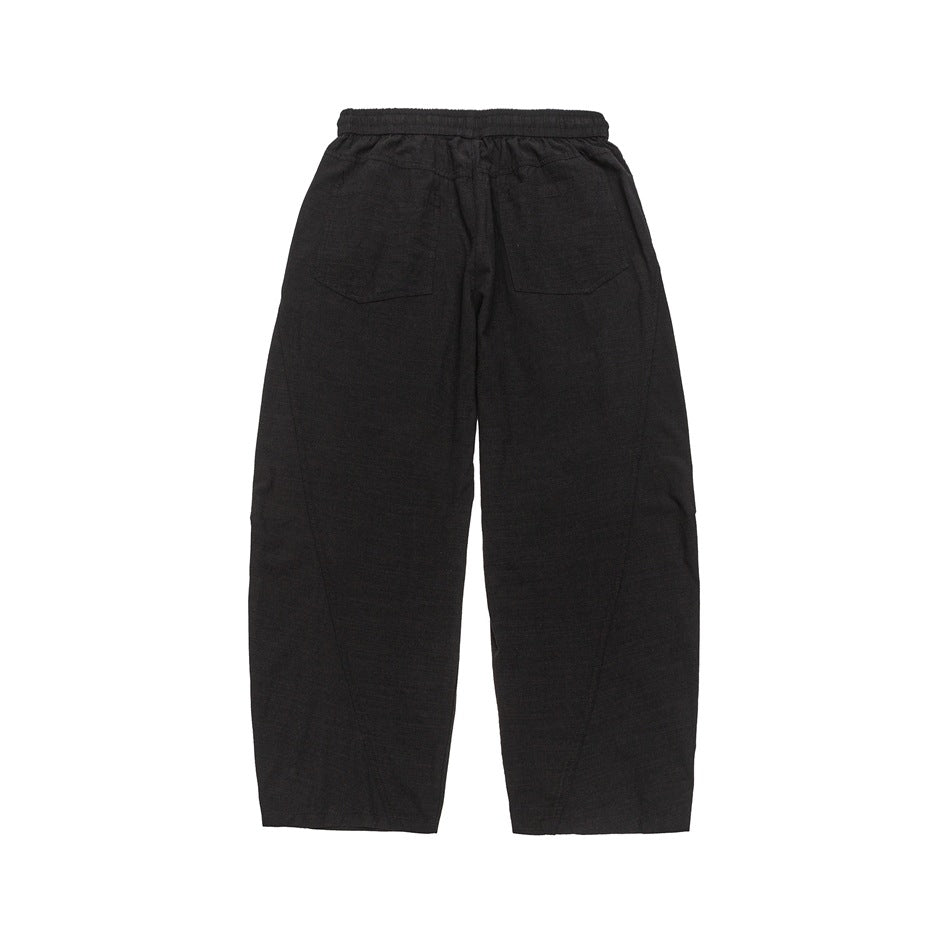 Back view of black relaxed pants with an elastic waistband and two patch pockets.