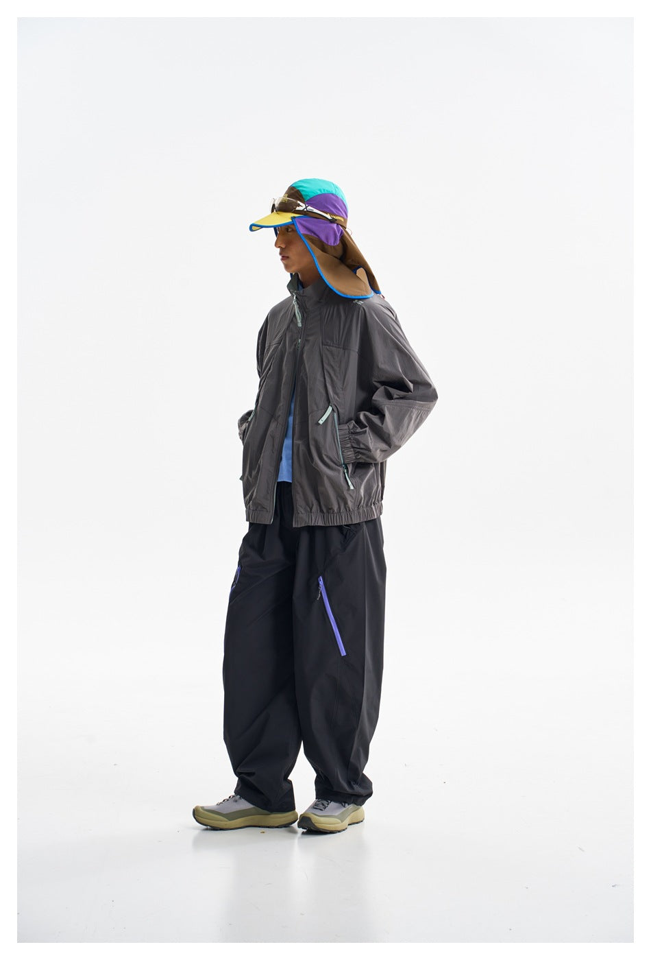 Side view of a model wearing a charcoal zip jacket, loose black trousers and a color-block sun hat.