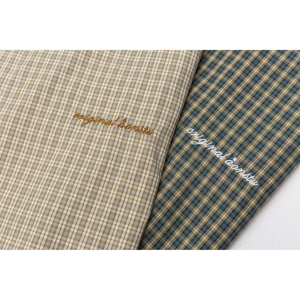 Close-up of two plaid shirts in cream and brown and teal and brown, each with cursive embroidery.