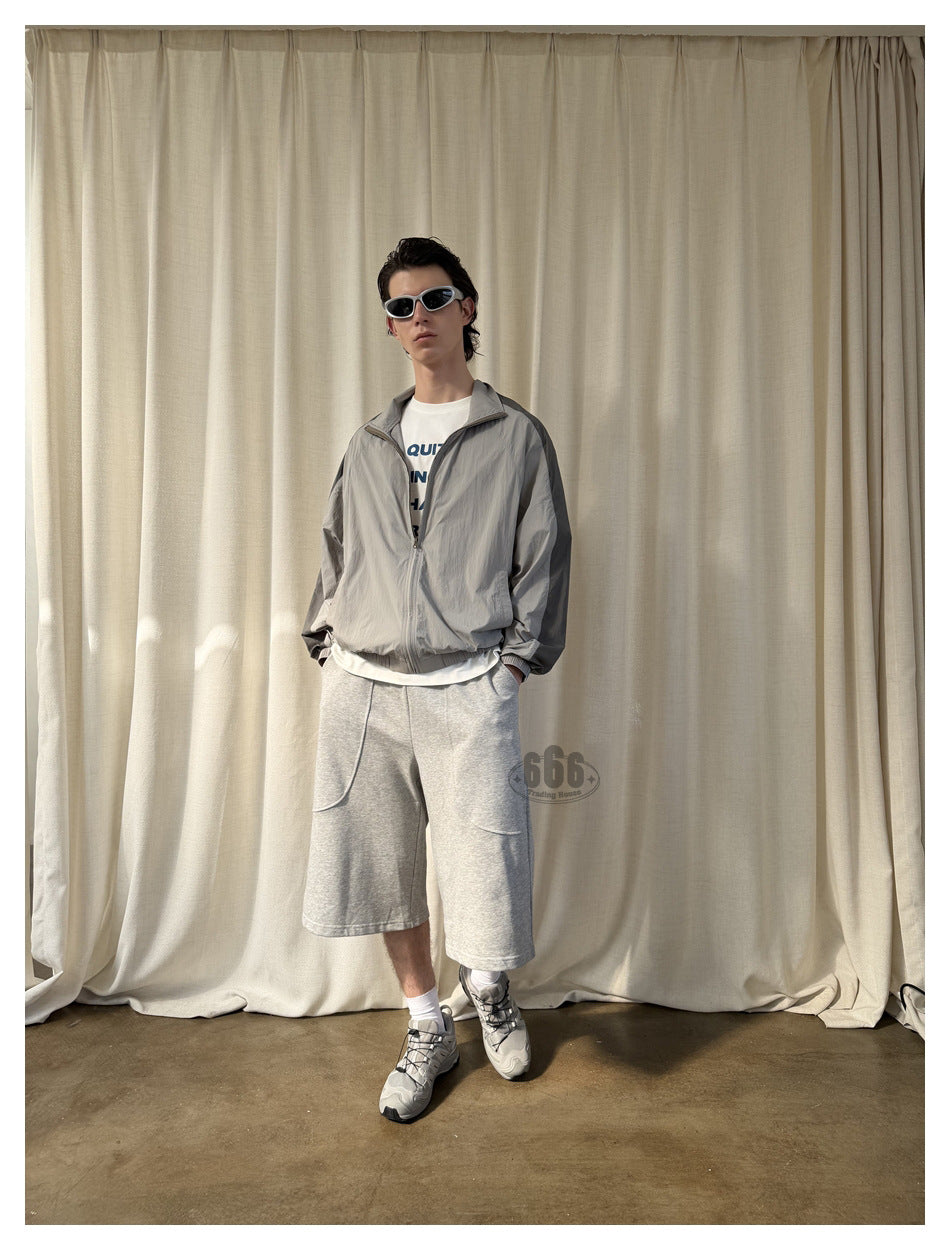 Model wearing loose light-gray knee-length shorts with curved pockets, paired with a gray zip jacket and white T-shirt.