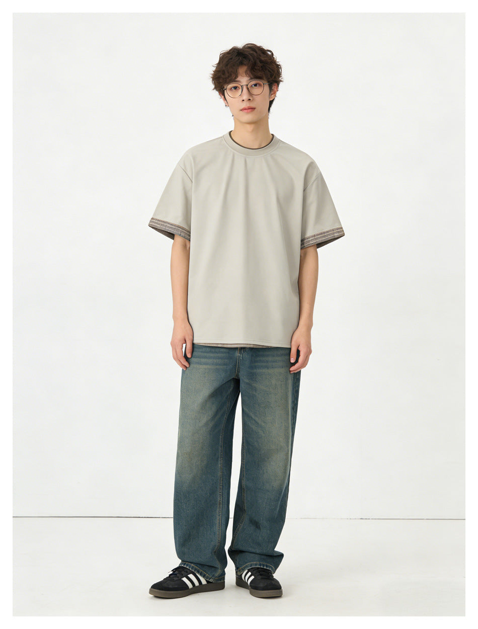 Model wearing a light beige short-sleeve crew-neck T-shirt with patterned sleeve trim and loose blue jeans.