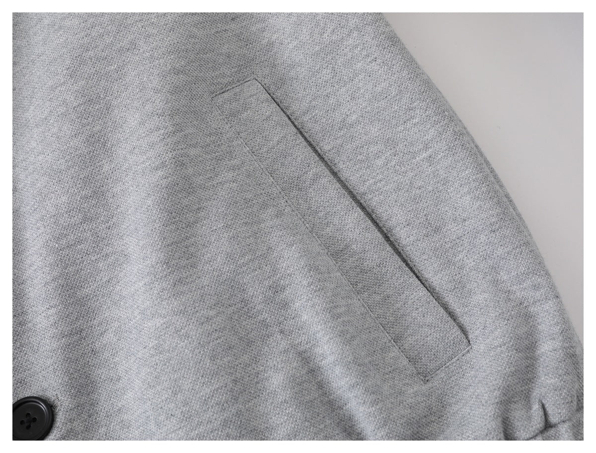 Close-up of a slanted welt pocket on a light gray jacket, with a black button at the edge.
