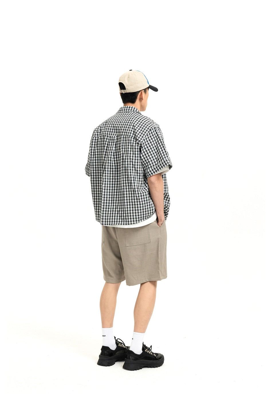 Back view of model wearing khaki shorts with a back patch pocket, plaid shirt, cap and black shoes