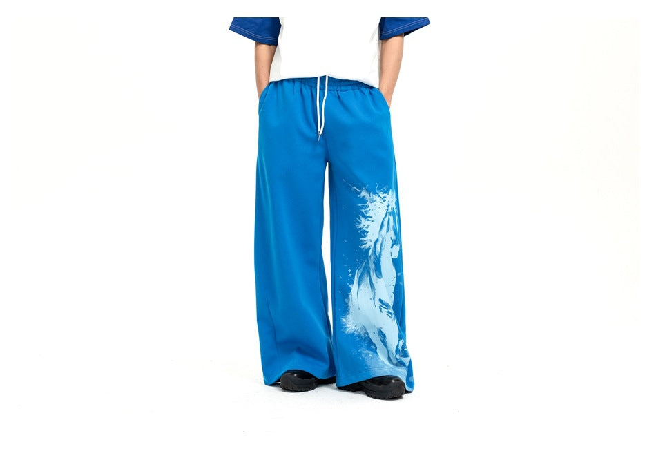 Model wearing bright blue wide-leg drawstring pants with a large white horse graphic on one leg, front view.