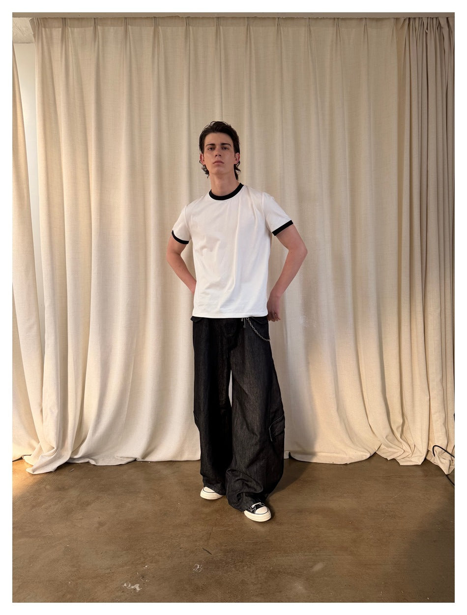 Model wearing a white short-sleeve T-shirt with black neck and sleeve trim, paired with loose black pants.