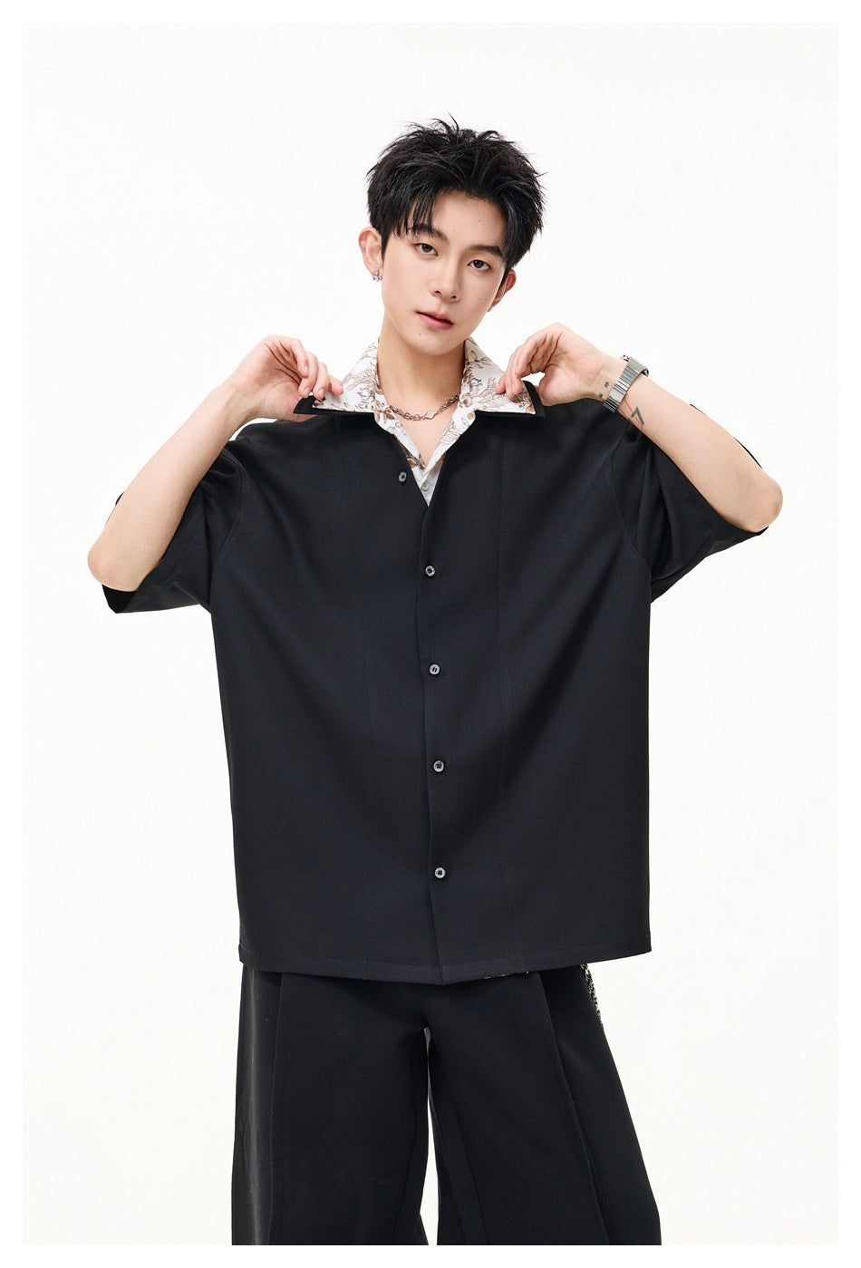 Front view of a model wearing a loose black short-sleeve button shirt over a white floral-collar top.