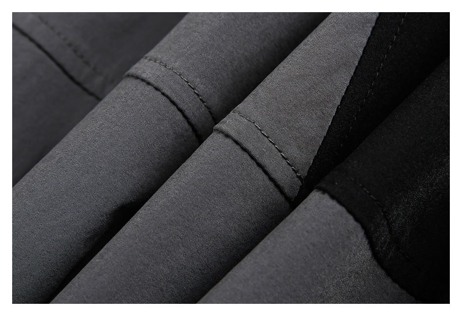 Close-up of charcoal gray and black garment fabric with several stitched folds and seams.