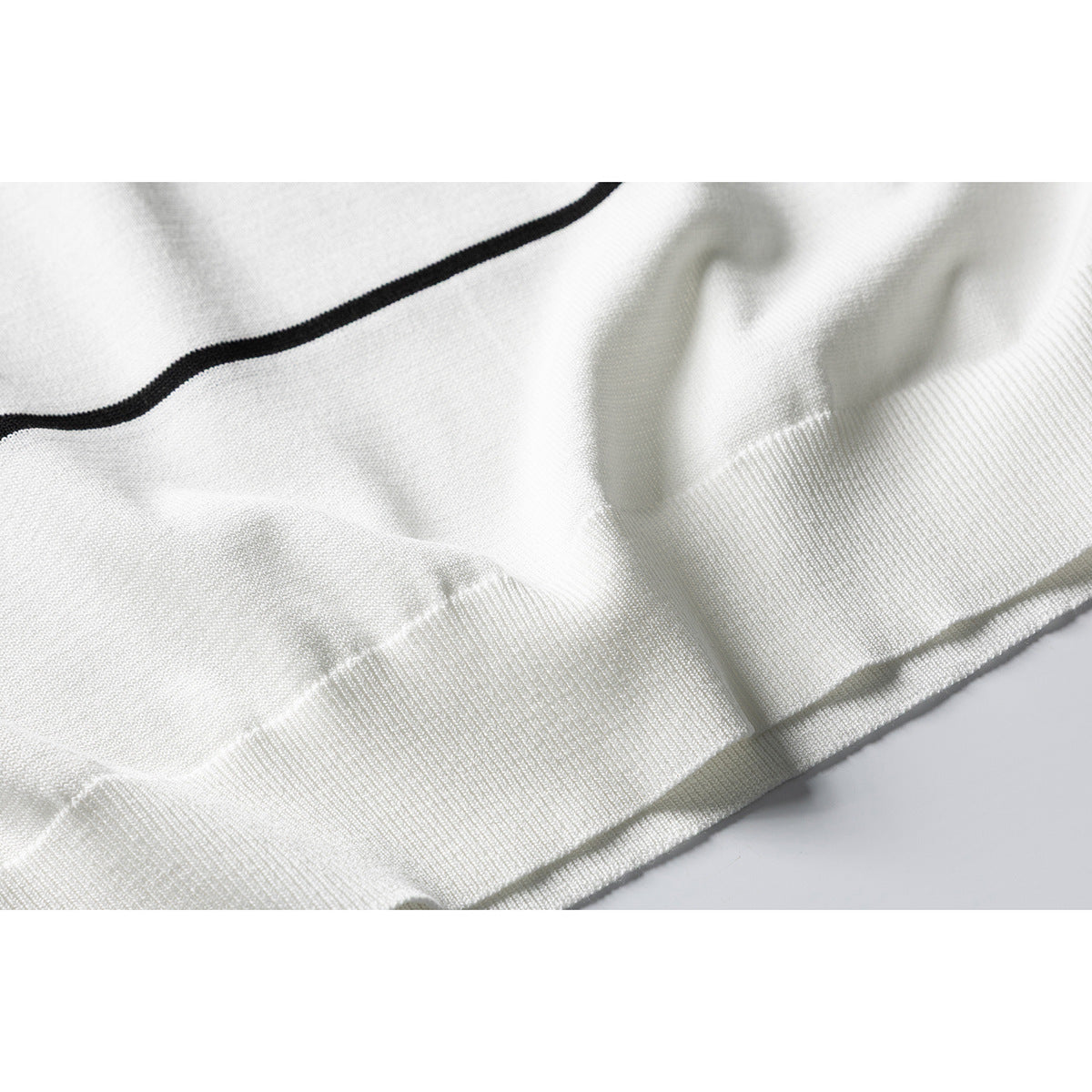 Close-up of an ivory knit top's black stripe and ribbed hem.