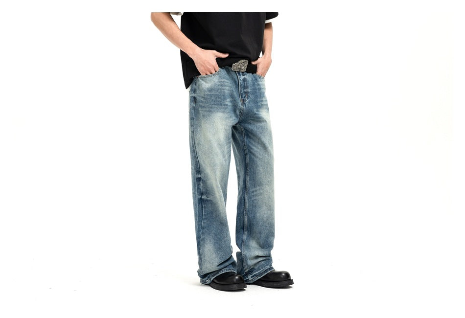 Cropped model wearing loose faded blue jeans with a black T-shirt and decorative belt buckle against white.