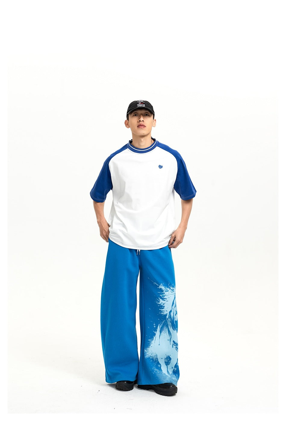 Model wearing a white-and-blue raglan T-shirt and wide-leg blue pants with a pale graphic on one leg.