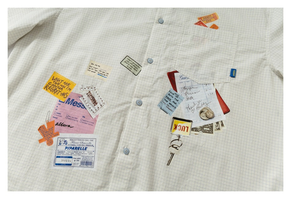 Flat-lay front of a cream, blue-grid button-up shirt decorated with colorful paper-style graphic patches.