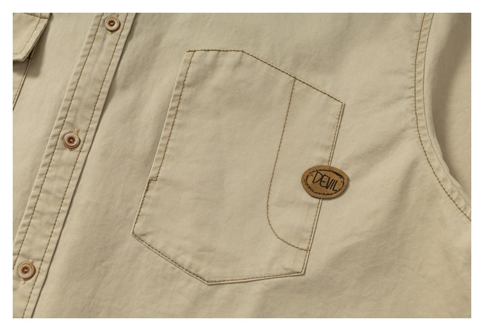 Close-up of a beige shirt chest pocket with a small brown DEVIL patch and nearby buttons.