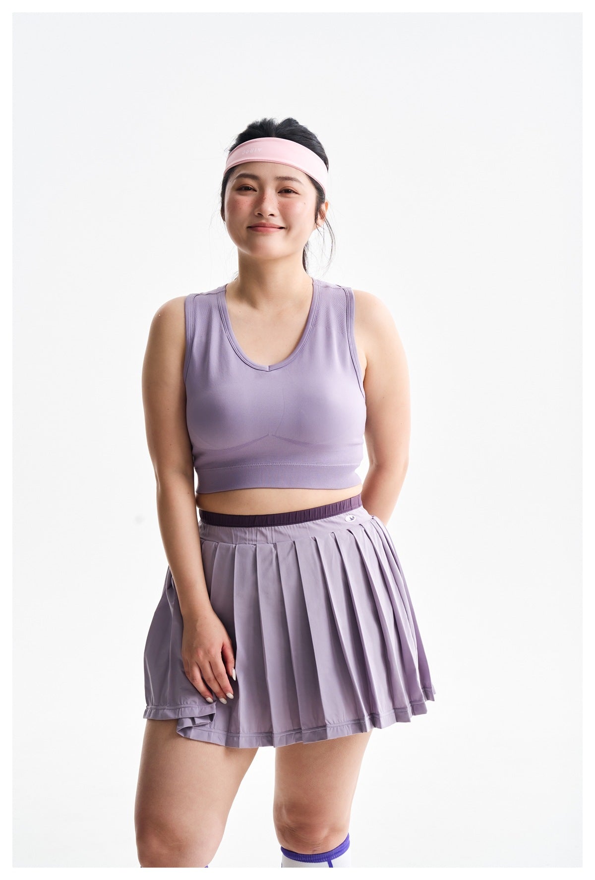 Model wearing a lavender sleeveless athletic top and pleated skirt, shown from the front against a white background.