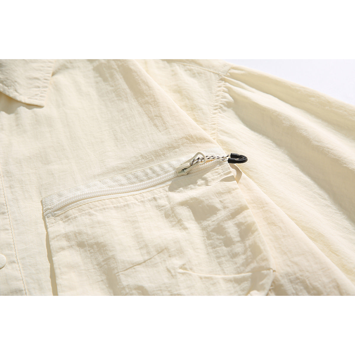 Close-up of a white zipper and black pull on an ivory shirt pocket.