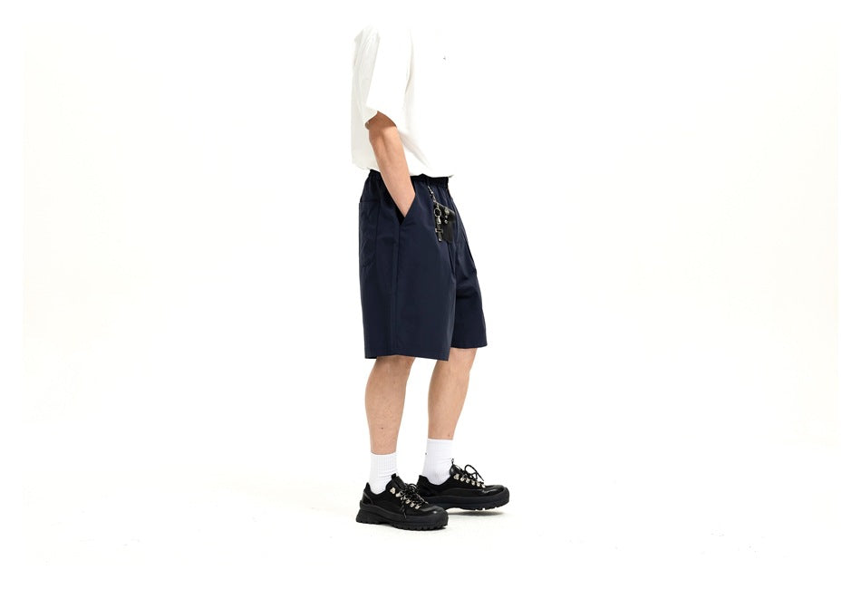 Side view of a model wearing navy knee-length shorts and a white T-shirt, with hands in the pockets.