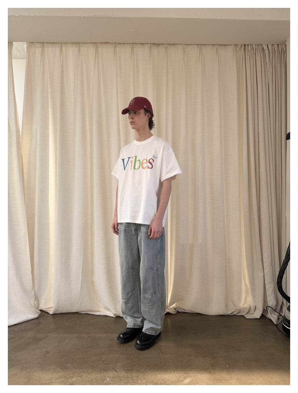 Model wearing the off-white Vibes T-shirt with light-wash wide-leg jeans and a burgundy cap, front view