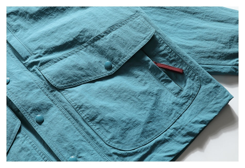 Close-up of a turquoise jacket's large flap pocket, snap button, and burgundy pocket detail.