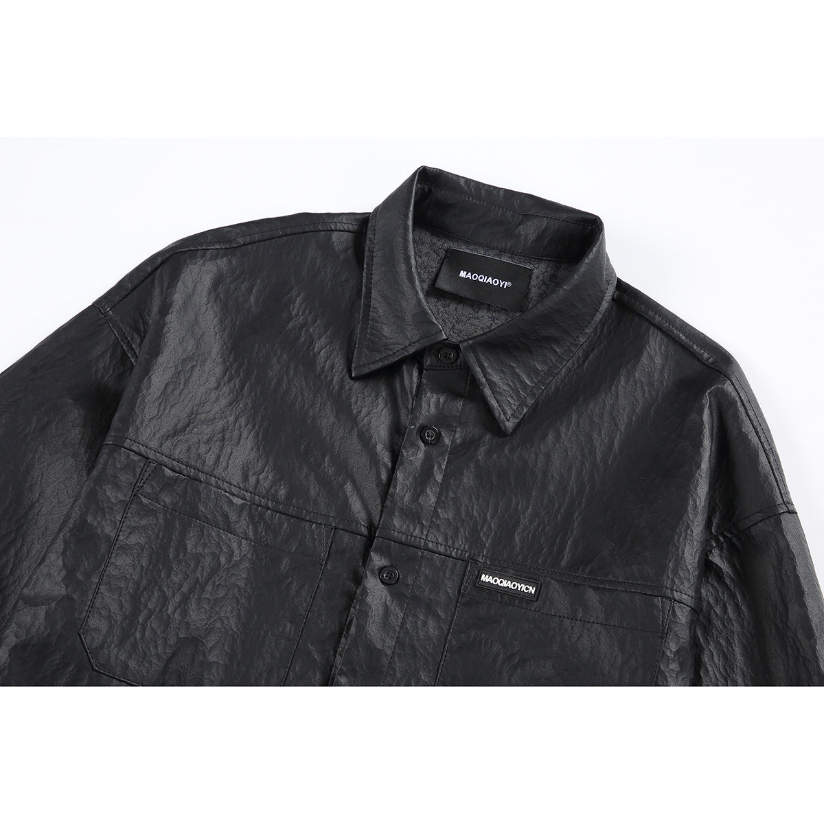 Close-up of a black crinkled button-up shirt with a pointed collar, chest pocket, and small sewn-on logo patch.