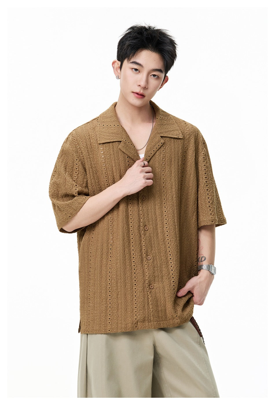 Close view of a model wearing a brown short-sleeve eyelet shirt with a notched collar and beige trousers.
