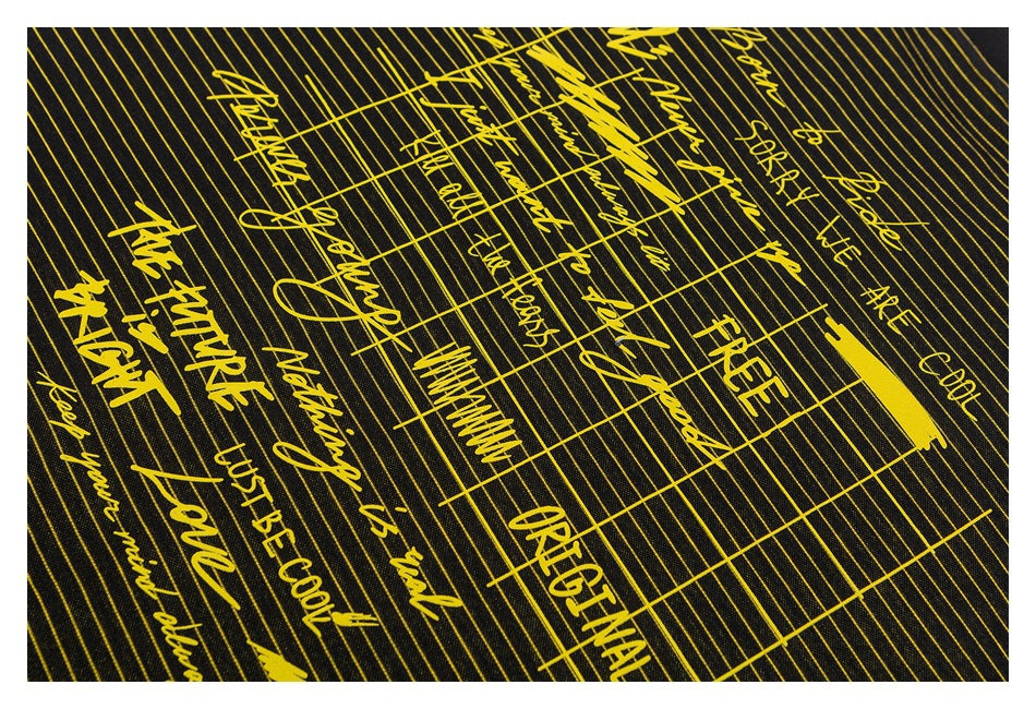 Close-up of yellow English lettering and grid-like graphics printed over thin yellow stripes on black fabric.
