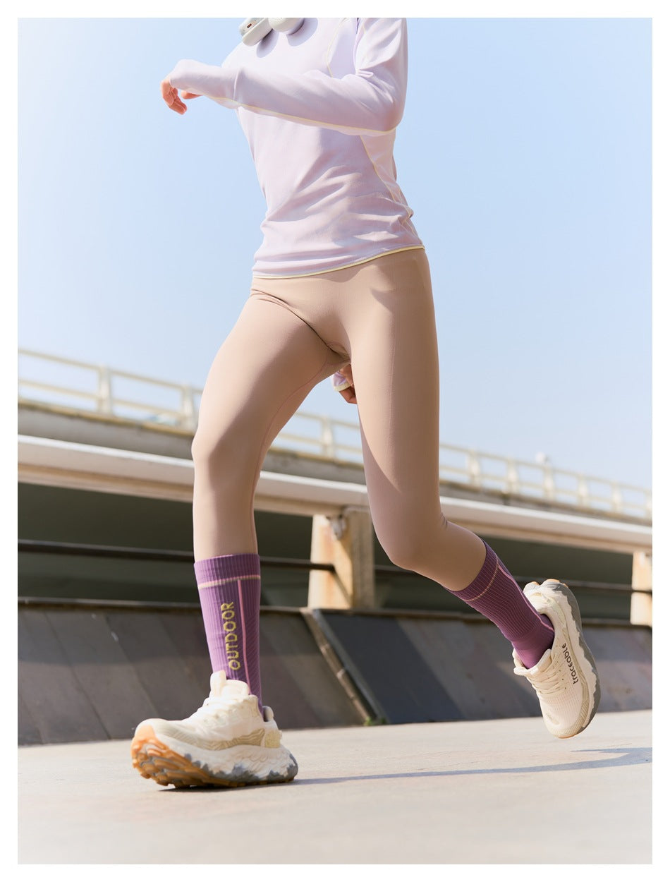 Cropped action view of a runner wearing a pale pink top, beige leggings, and purple socks.