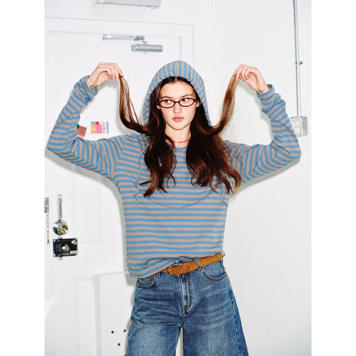 Close view of a model in a blue and taupe striped hooded top, holding her hair out to either side.