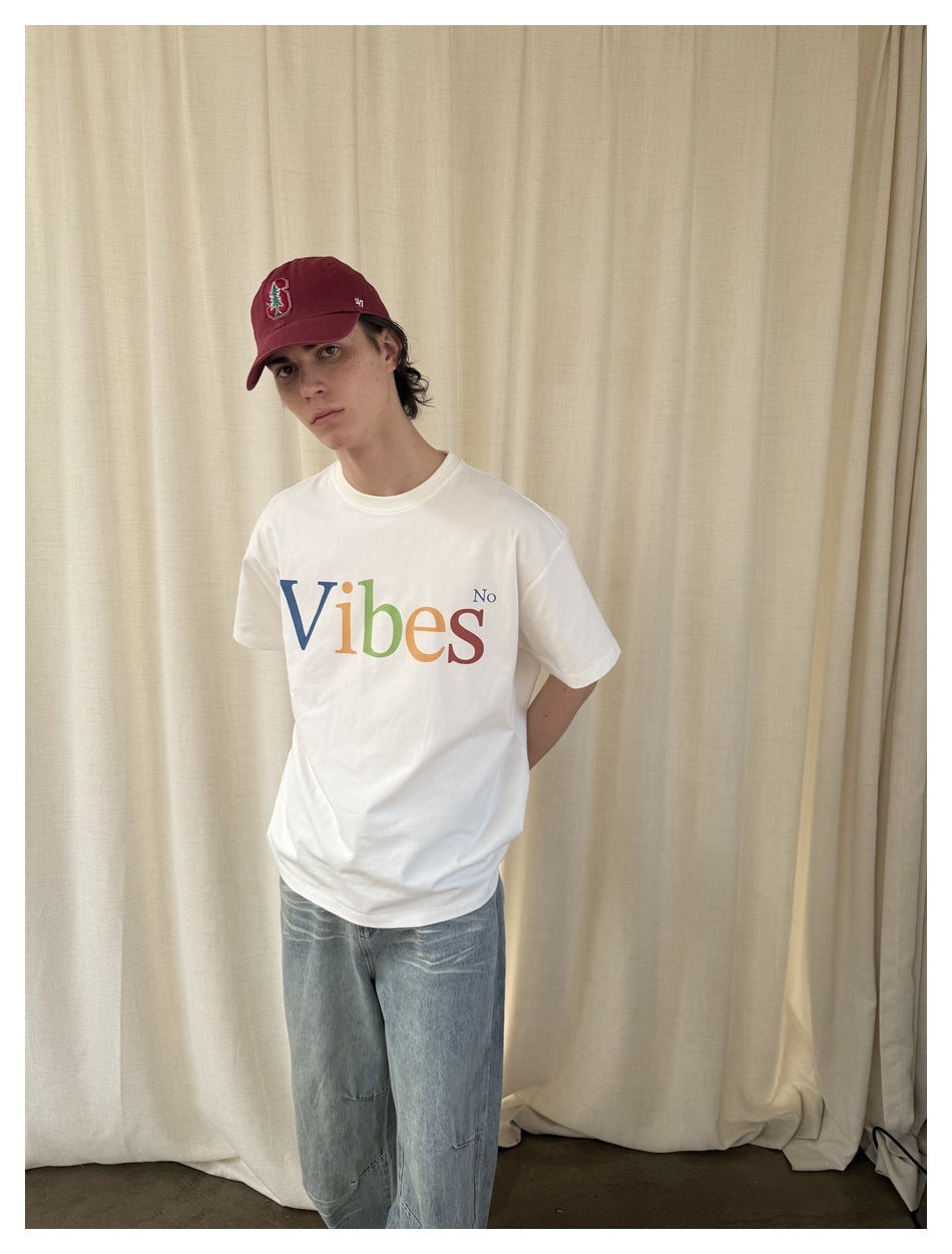 Closer front view of a model wearing a white T-shirt with multicolored “Vibes No” lettering and light-wash jeans.