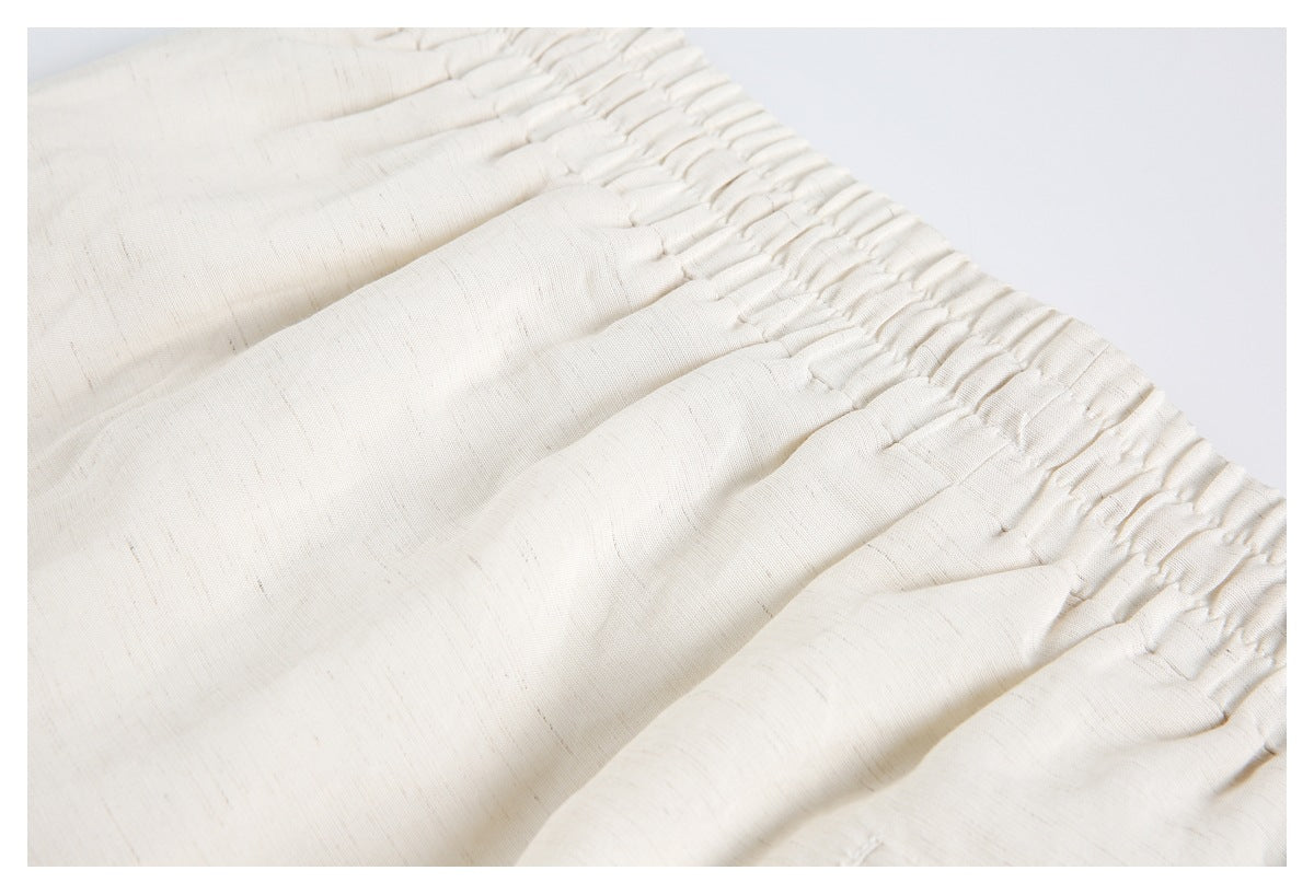 Close-up of the gathered elastic waistband and pleats on cream trousers.