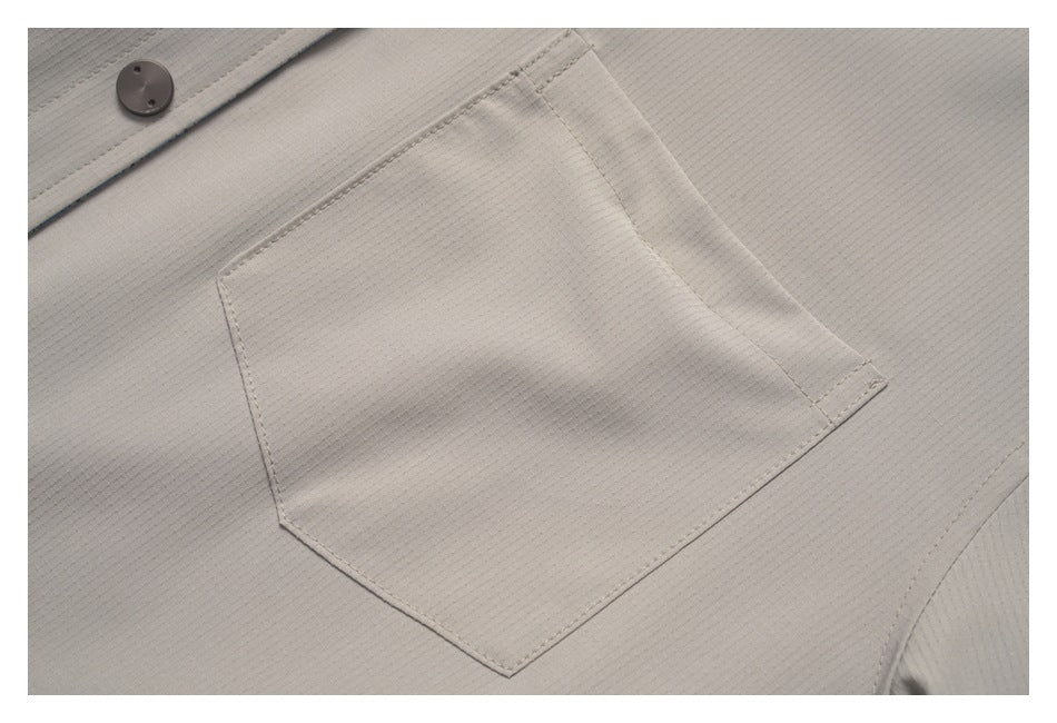 Close-up of a large stitched chest pocket on light taupe fabric, with a dark button near the edge.