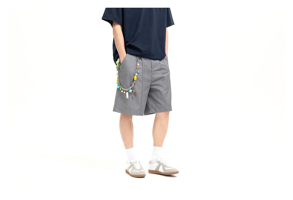 Cropped angled view of a model wearing gray pleated shorts with a colorful charm chain and a navy T-shirt.