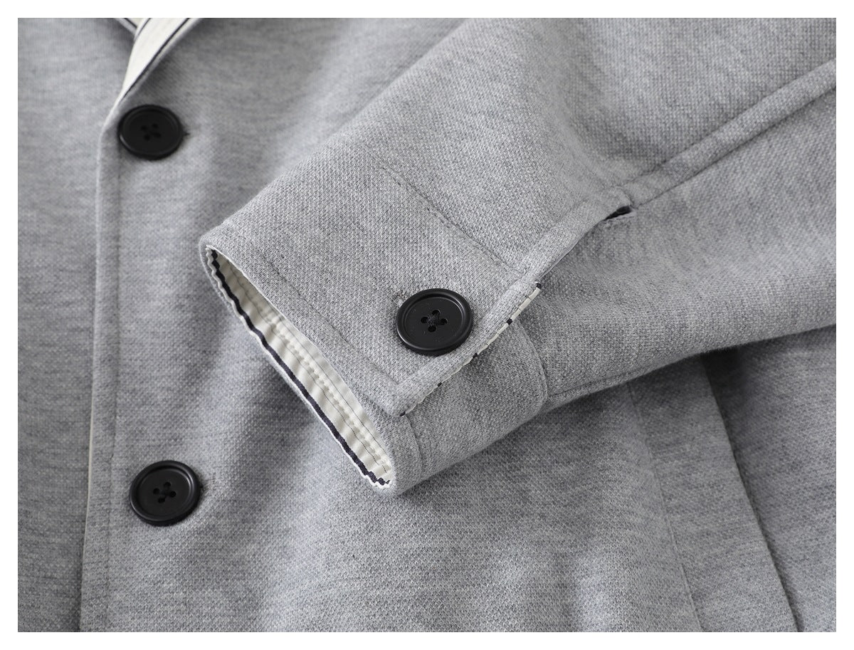 Close-up of a light gray jacket sleeve cuff with a black button and striped lining visible at the edge.