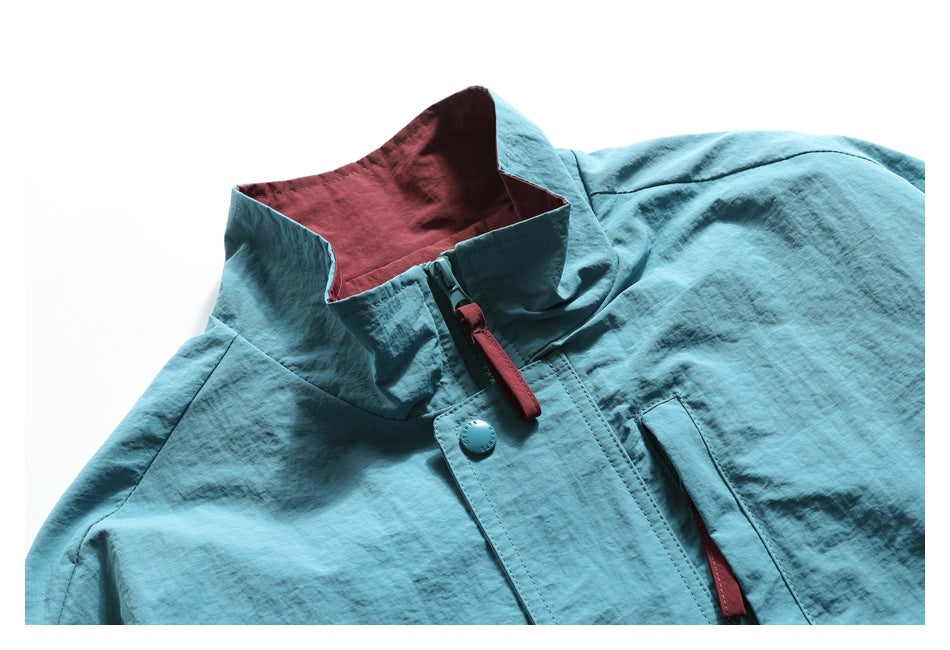 Close-up of a turquoise jacket's raised collar, burgundy lining, zipper pull, and snap-front placket.