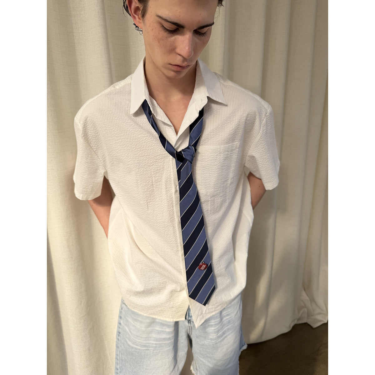 Close view of a model in a textured white short-sleeve shirt with a chest pocket and navy striped tie.