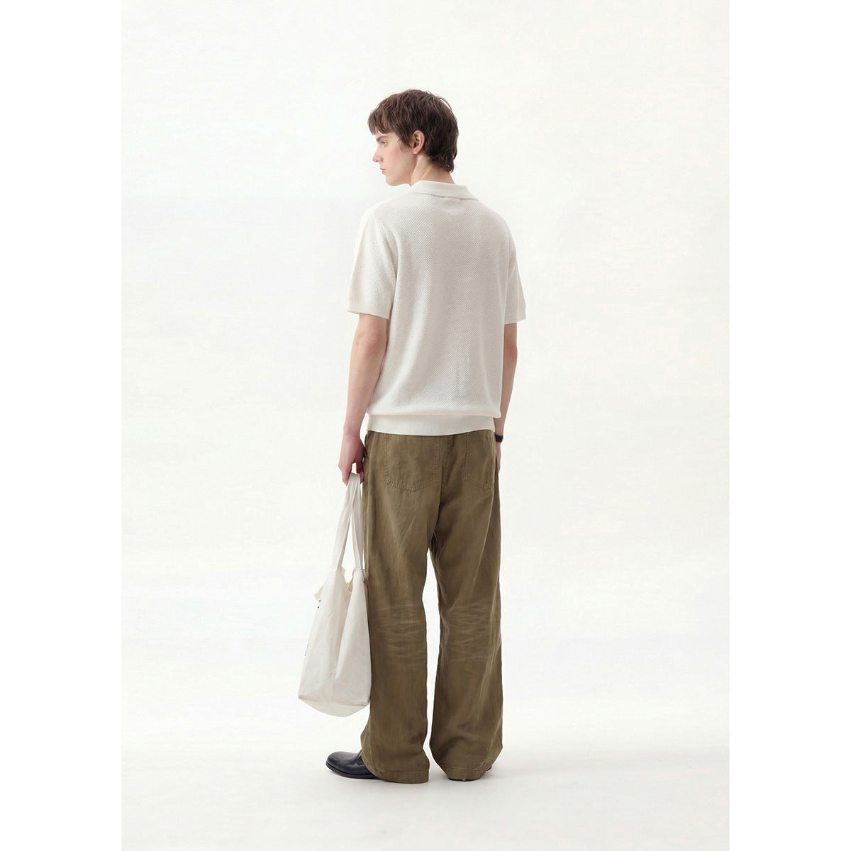 Rear view of a model wearing an ivory short-sleeve collared pullover with olive wide-leg trousers.