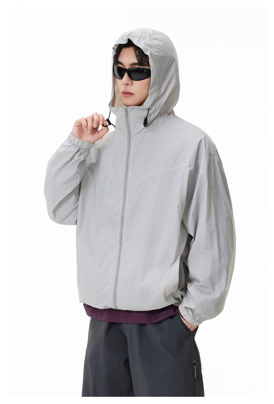Close view of a model wearing a light gray hooded zip jacket with the hood up and drawcords visible.