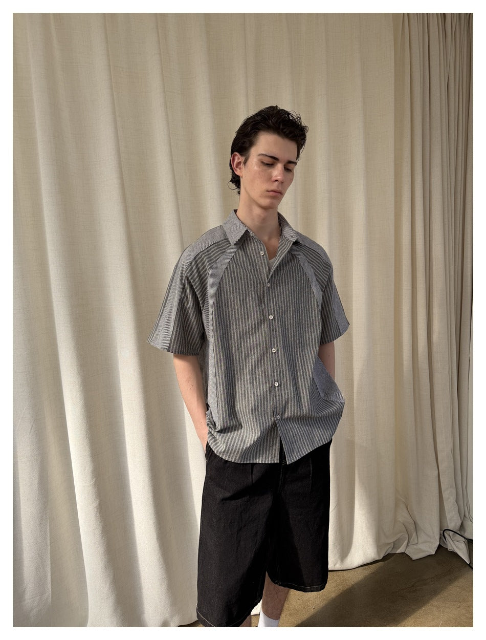 Front view of a model wearing a gray striped short-sleeve button-up shirt with black shorts.