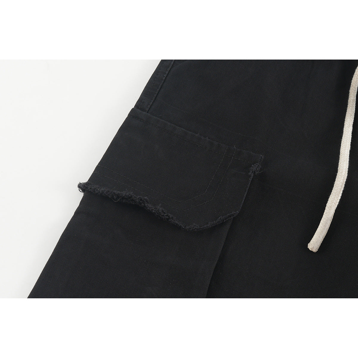 Close-up of a black shorts cargo pocket with a frayed edge and an off-white drawstring.