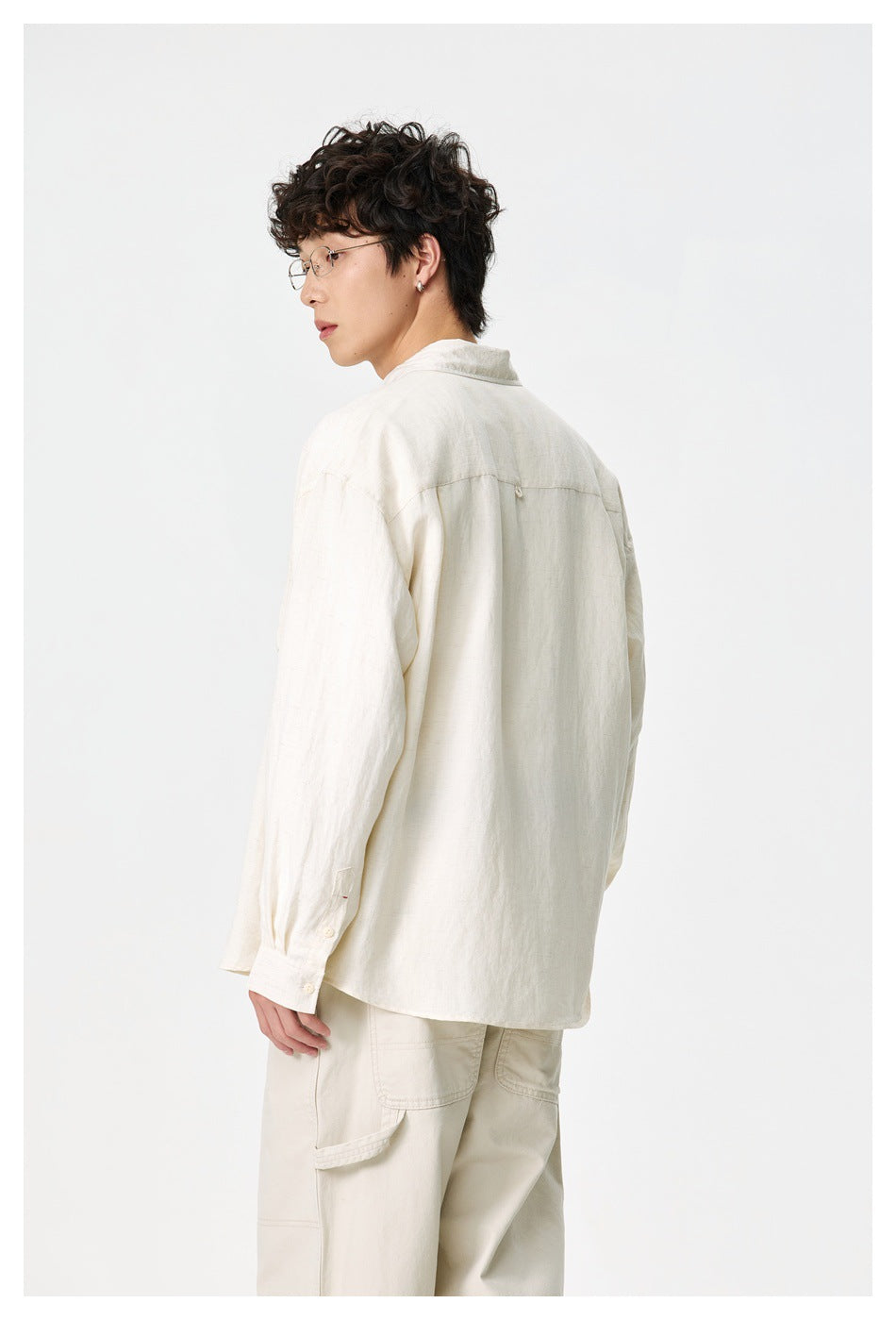 Rear view of a model wearing an ivory long-sleeve button-up shirt with a yoke seam and cream trousers.