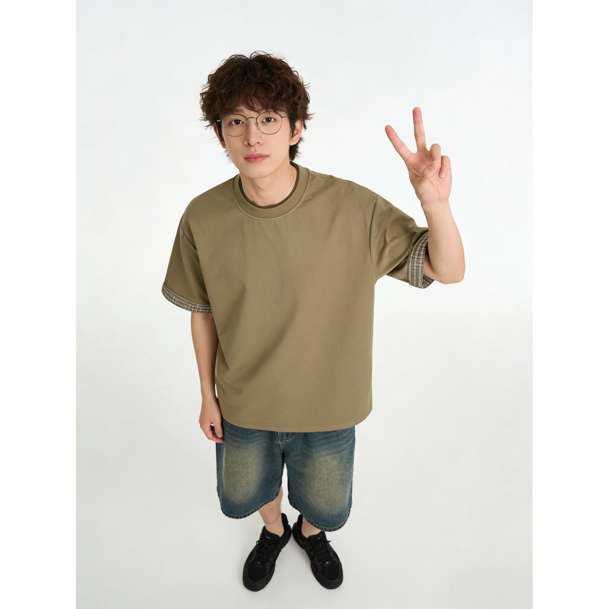 Close view of a model wearing an olive-brown T-shirt with checked sleeve cuffs and a contrast neckline.