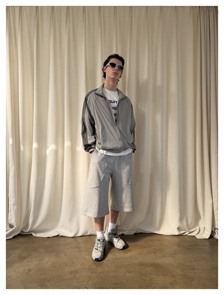 Full-length view of a model wearing light-gray knee-length shorts with curved pockets and a gray zip jacket.