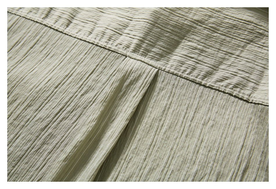 Close-up of a stitched seam and fabric panels on the muted olive-gray striped shirt.