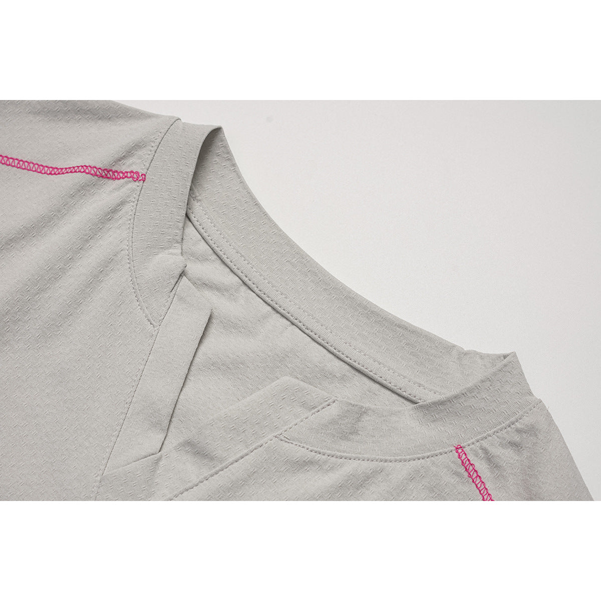 Close-up of a light gray top's neckline and shoulder, showing pink overlock stitching and a small V-shaped insert.