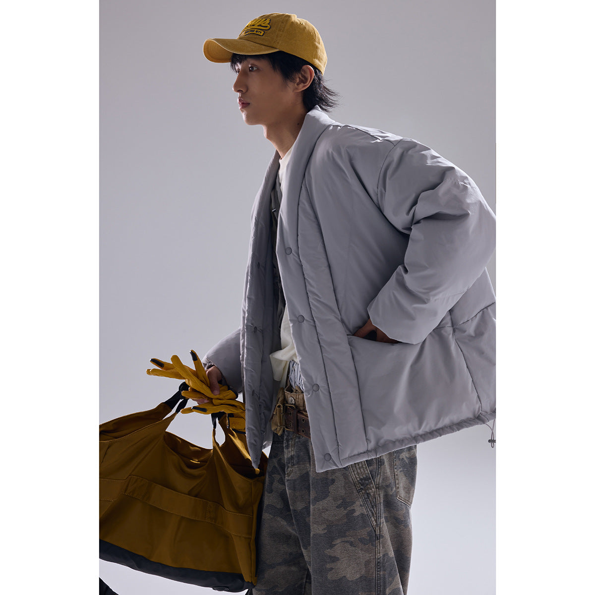 Model wearing a light gray oversized quilted jacket with snap buttons and large pockets, paired with camouflage pants.