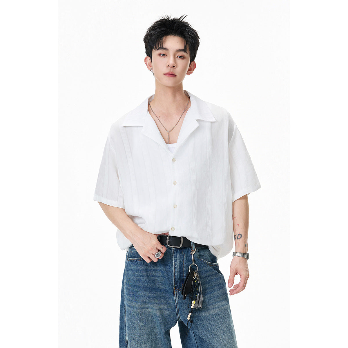 Model wearing a loose white short-sleeve open-collar shirt with blue jeans.
