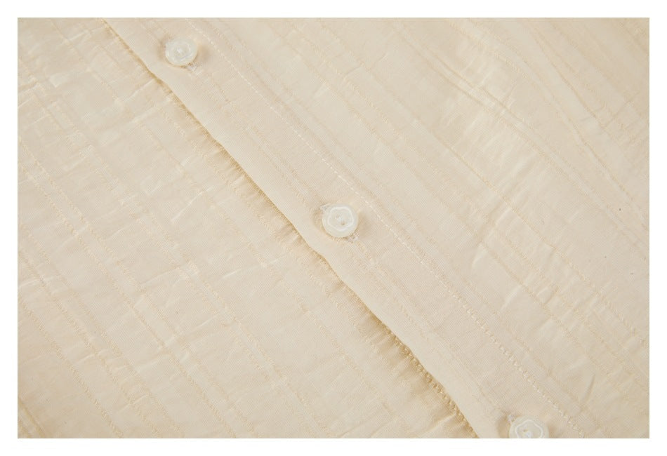Close-up of an ivory shirt's front placket with white buttons and subtle vertical textured stripes.