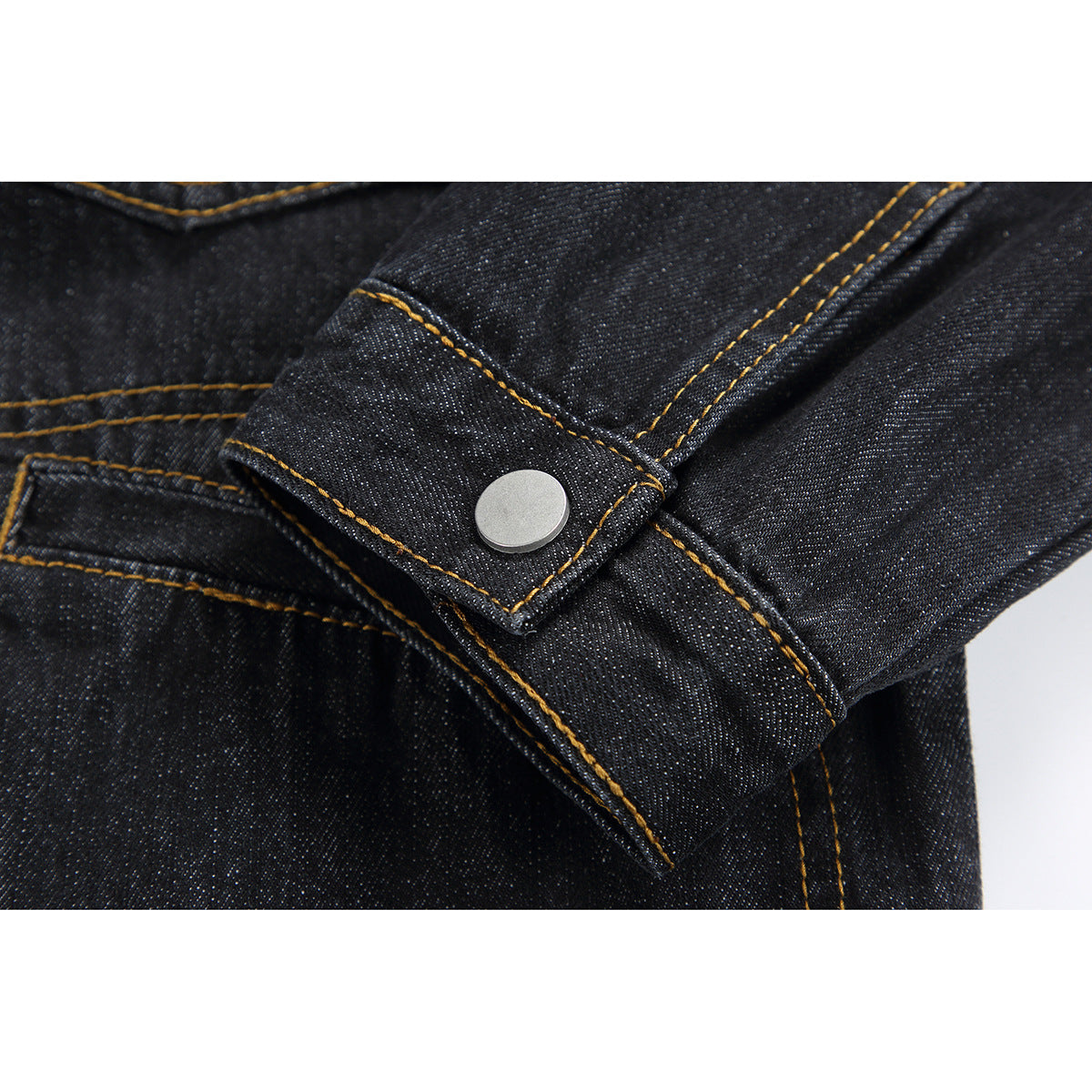 Close-up of a black denim jacket cuff with a silver snap and contrasting gold stitching.
